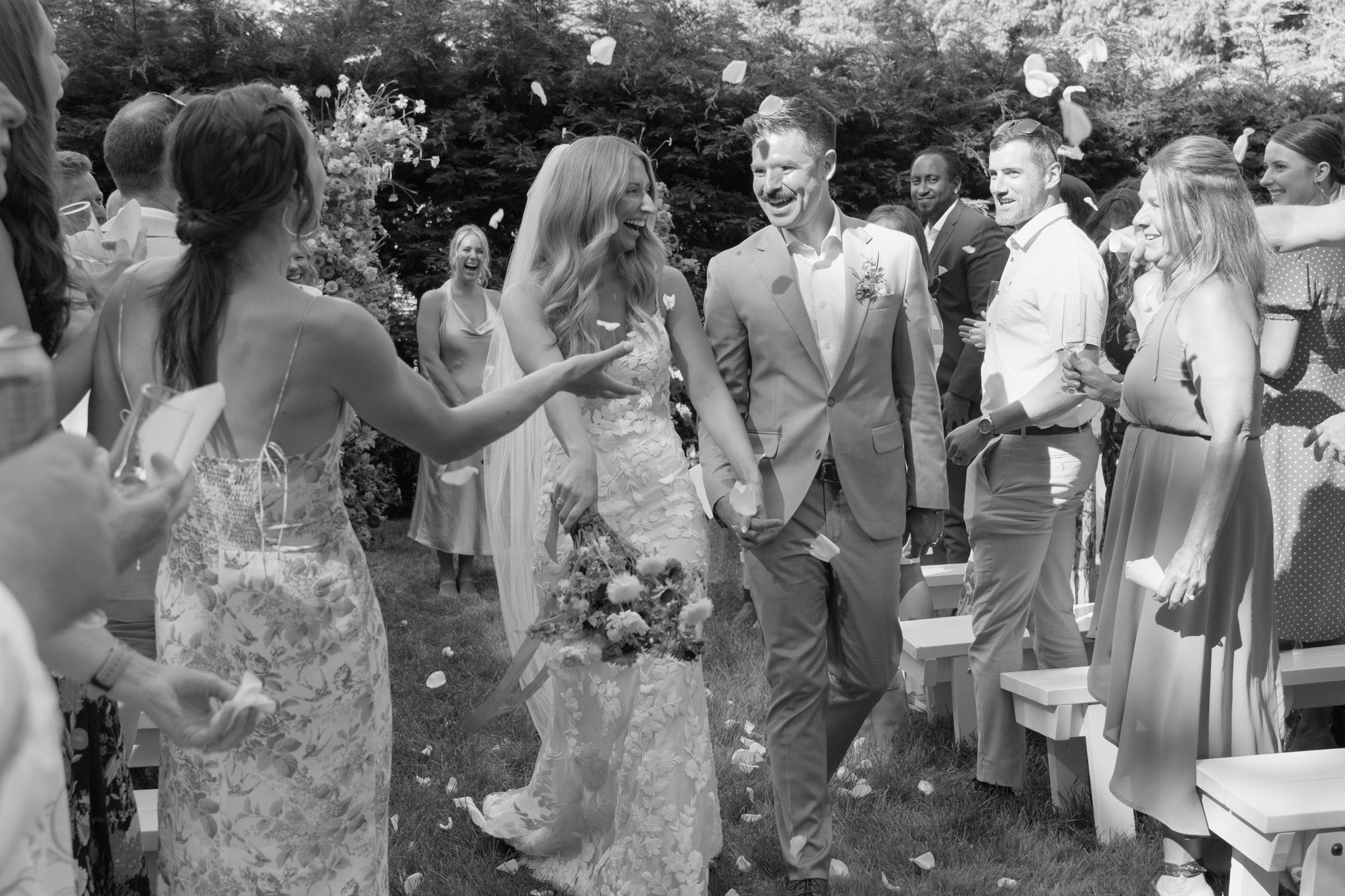bride and groom walking back down the aisle smiling, surrounded by friends and family - Photographer: Laryssa at Captured by LK