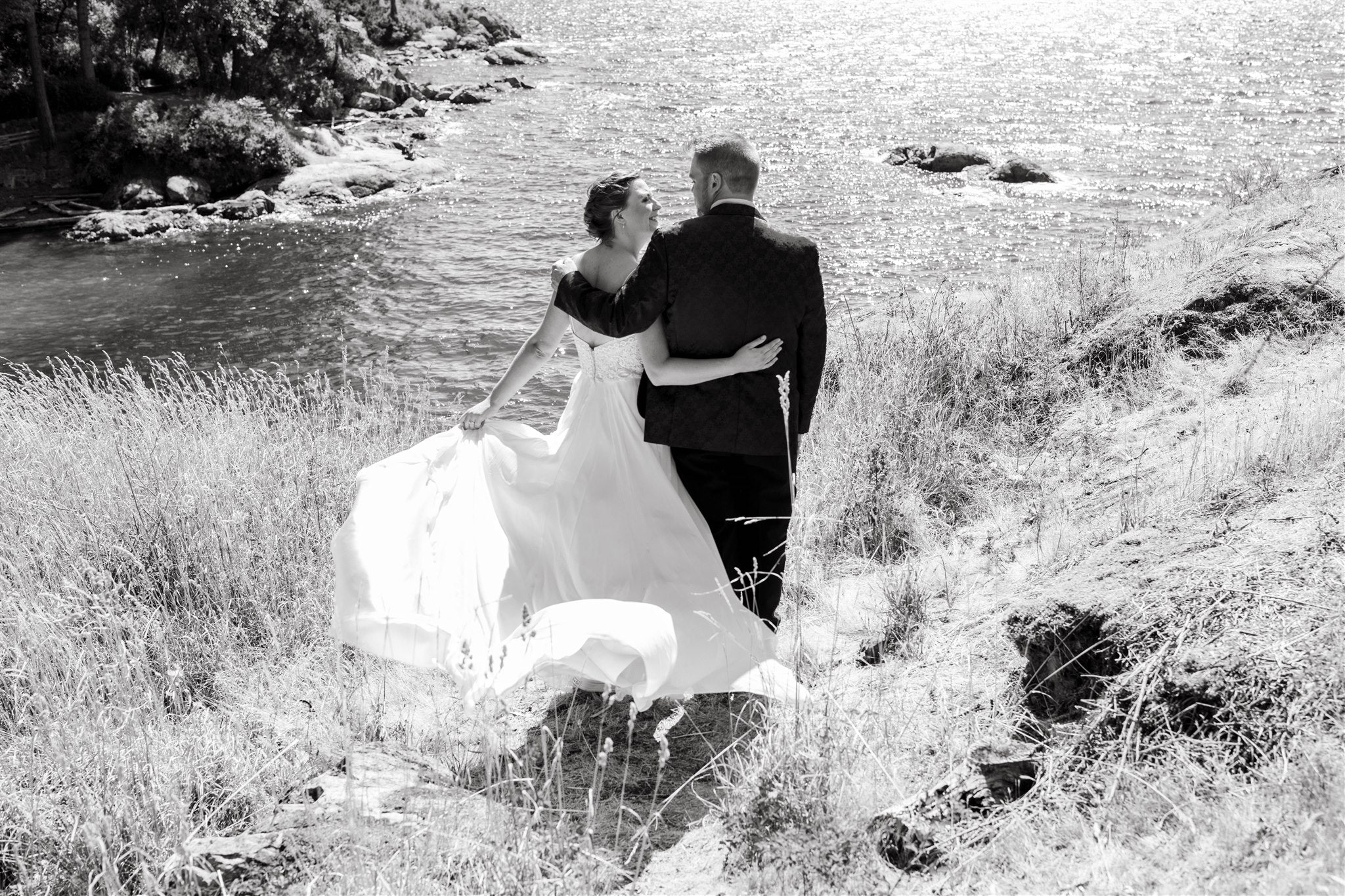 bride and groom standing arm in arm in front of the water