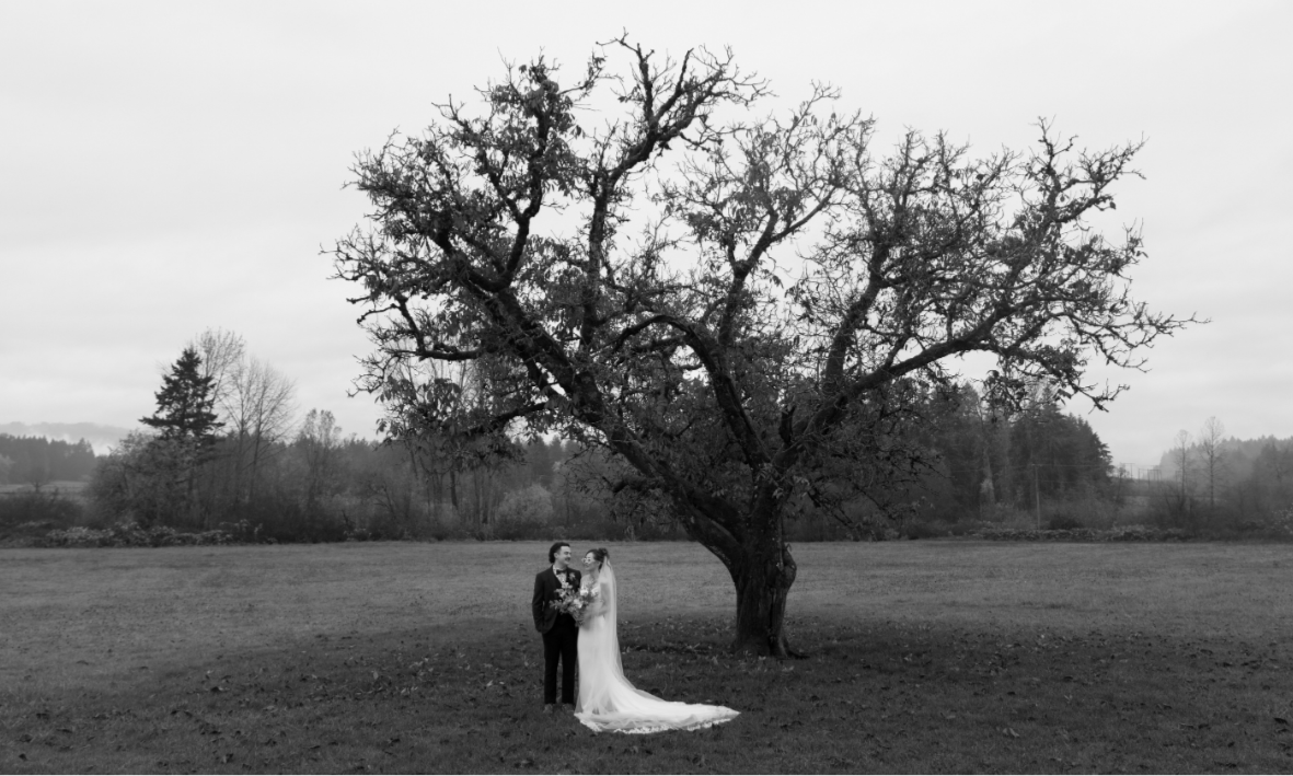 Black and white photo of a wedding couple standing under a large tree in a field. Intended Events - Photo by Taylor Dawning Photography. Keating Farm, Vancouver Island