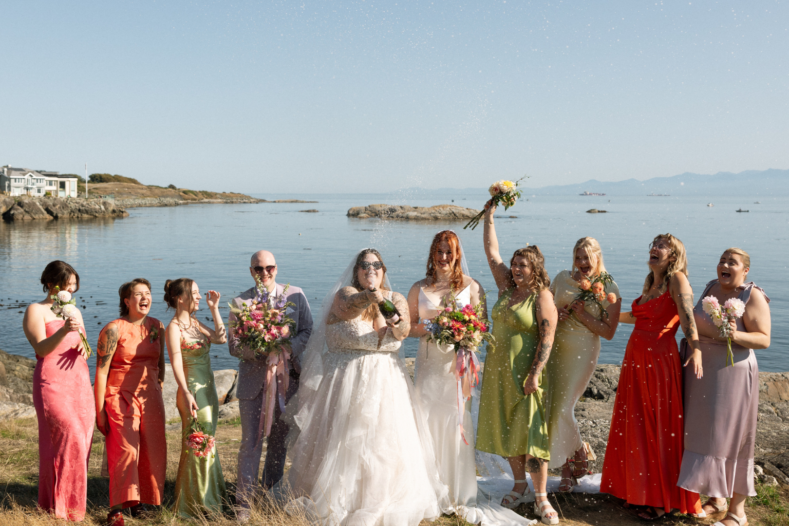 Wedding party celebrating at a Vancouver Island beach with champagne in colourful wedding attire - LGBTQ+ wedding - Victoria BC Wedding - Kiana Bryn Photography