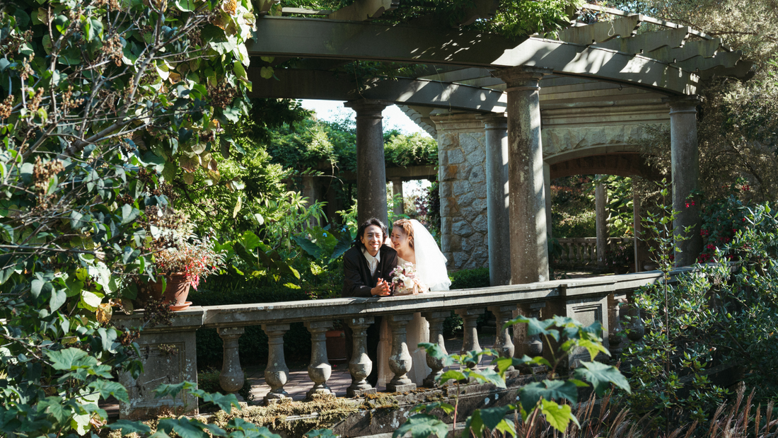 bride and groom leaning on a stone wall, surrounded by greenery in a garden - Hatley Castle, Rebeka Lucija Studio