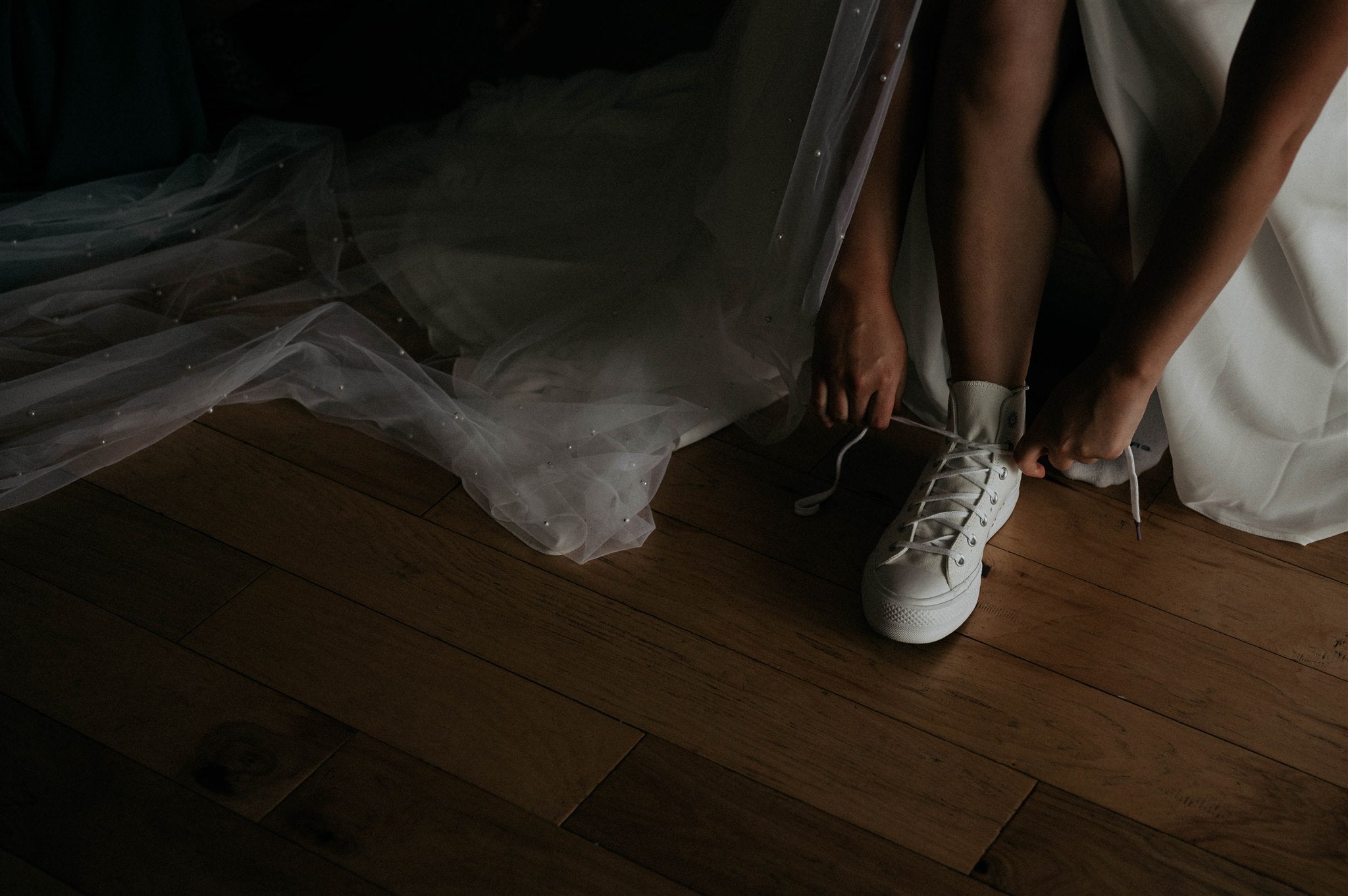 bride tying the shoelace of a sneaker below the tulle skirt of her dress