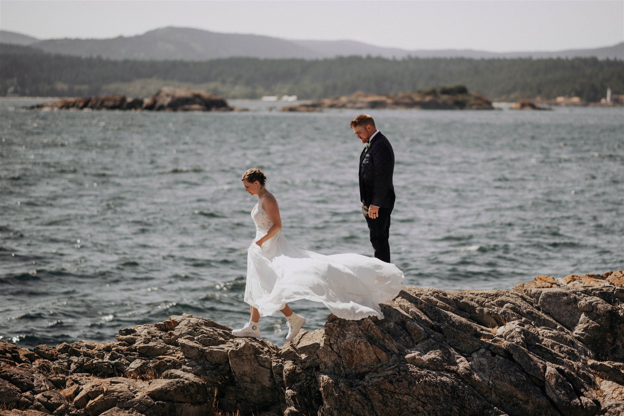 bride and groom climbing rocks along the ocean