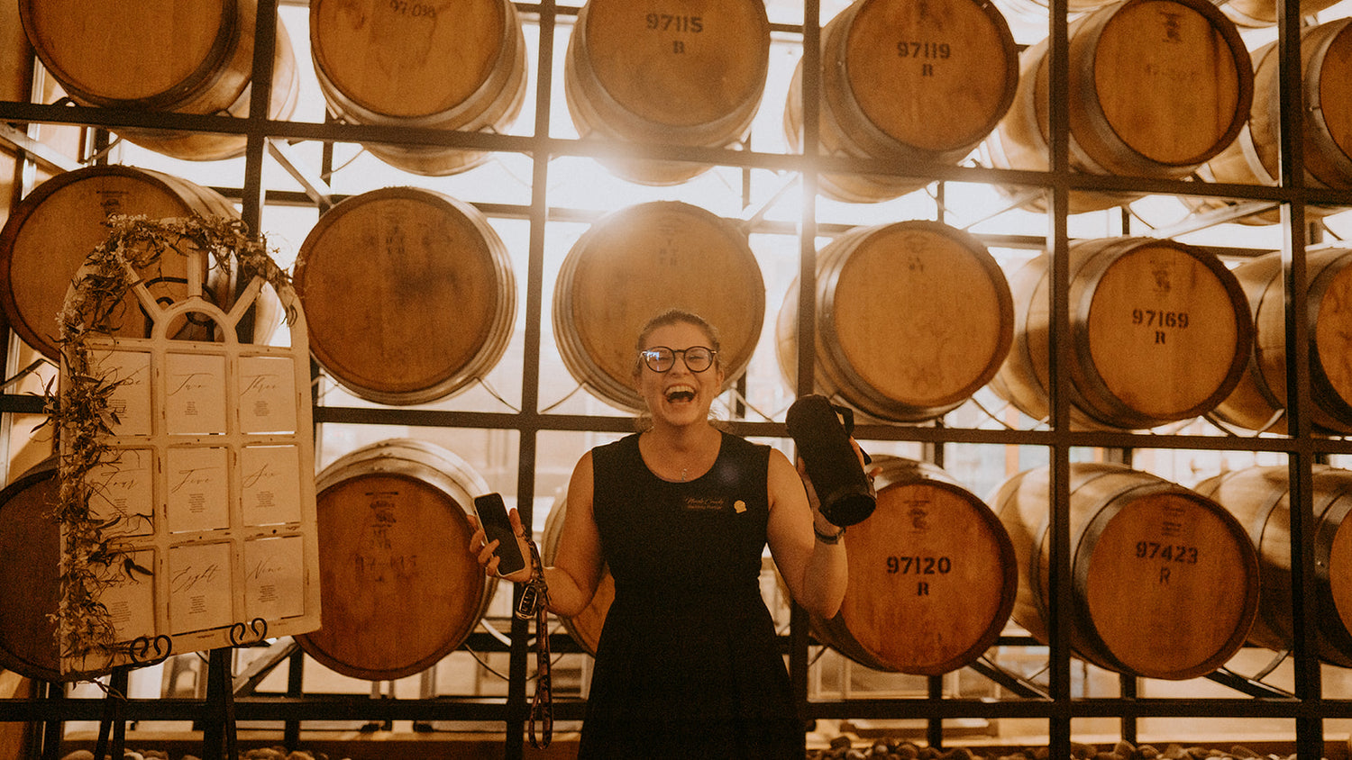 Nicole in a black dress laughing in front of a wall of wine barrels